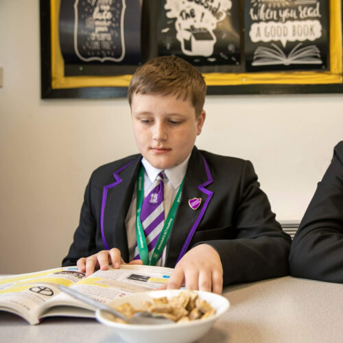 Two secondary-aged pupils reading and eating breakfast.