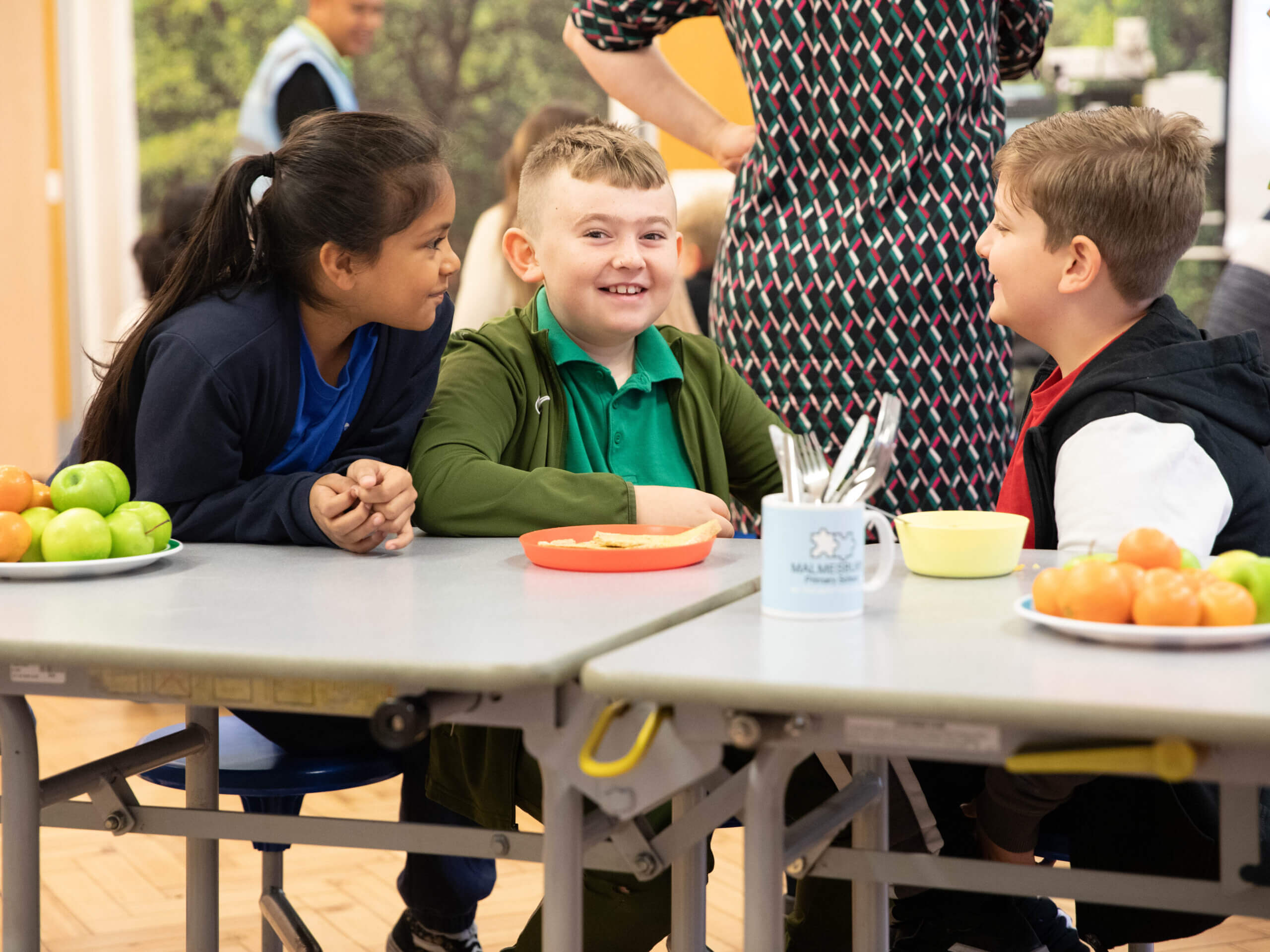 School aged children seated at a table eating breakfast and talking to one another