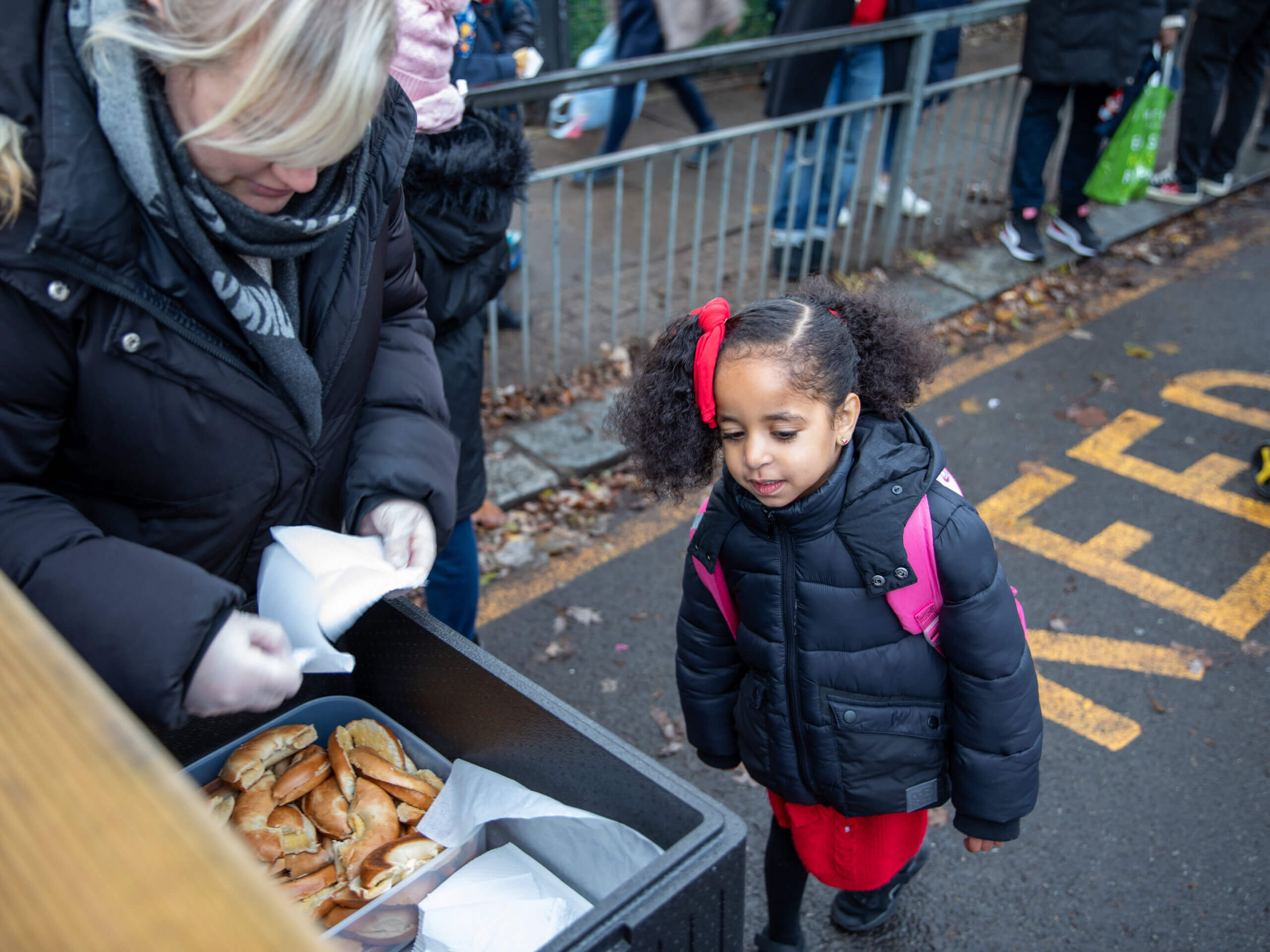 Image of a school aged child awaiting to receive a breakfast bagel from an adult